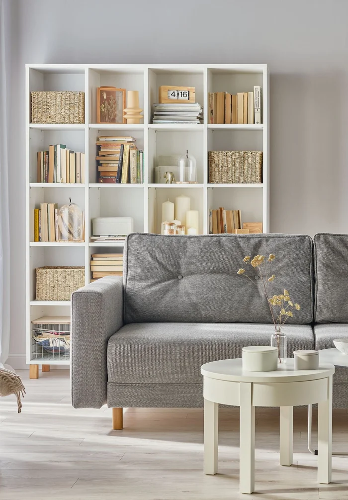 Minimalistyczny salon z szarą sofą i białym regałem.